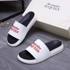 Pair of white slide sandals with black footbeds and red Alexander McQueen logo straps.