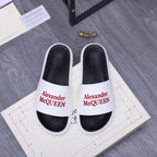 White slide sandals with black footbed and Alexander McQueen logo strap.