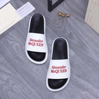 White slide sandals with black footbeds and red Alexander McQueen logo on straps.