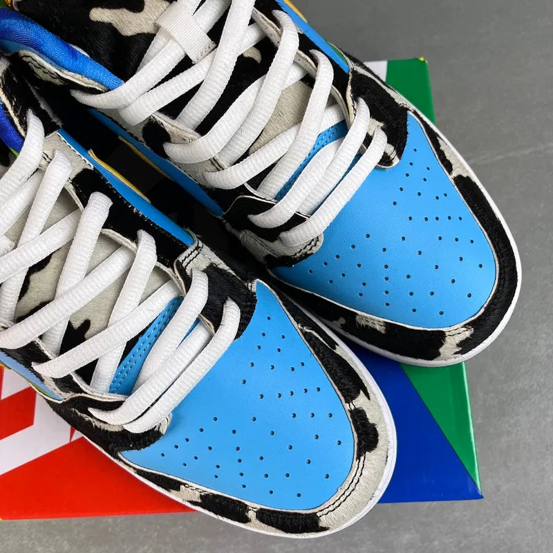 SB Dunk Low lace-up sneaker close-up: white laces, blue quarter panels, cow print