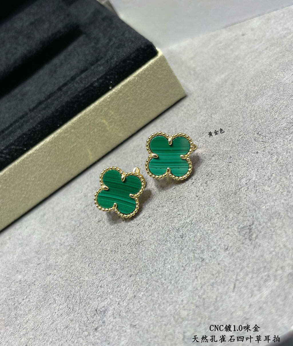 Green enamel four-leaf clover stud earrings with gold-tone frames on surface.
