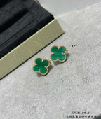 Green enamel four-leaf clover stud earrings with gold-tone frames on surface.