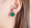 Green enamel four-leaf clover stud earring on an earlobe.