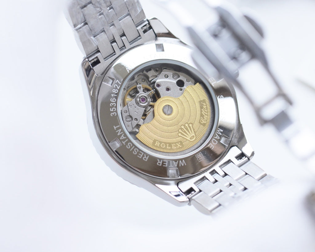 Rolex watch open caseback view with visible movement, silver metal bracelet