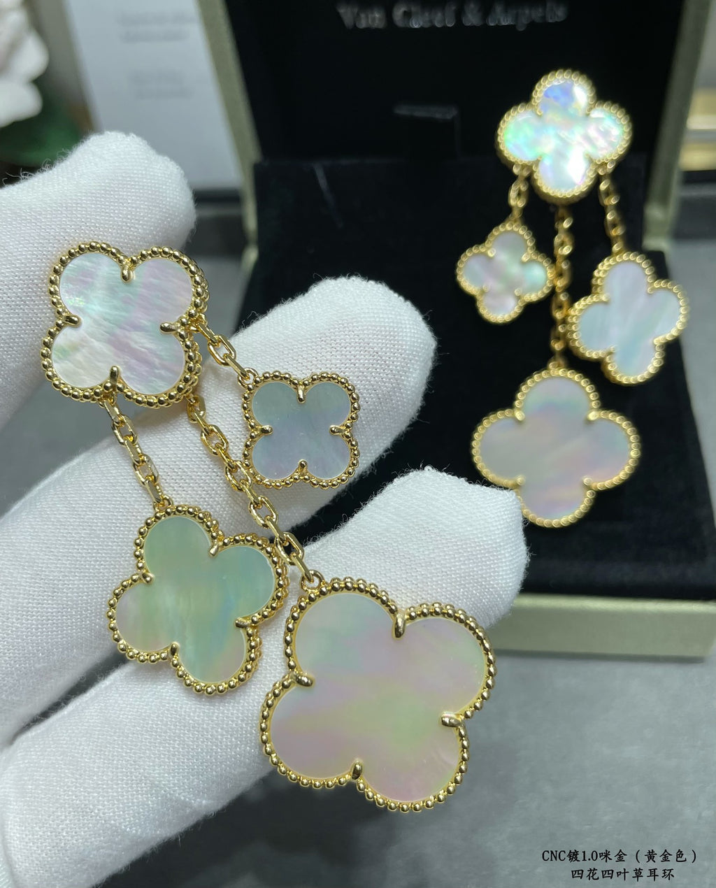 Gold-tone clover dangle earrings with mother-of-pearl charms on white glove