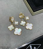 Gold-tone clover dangle earrings with iridescent mother-of-pearl charms on gray surface