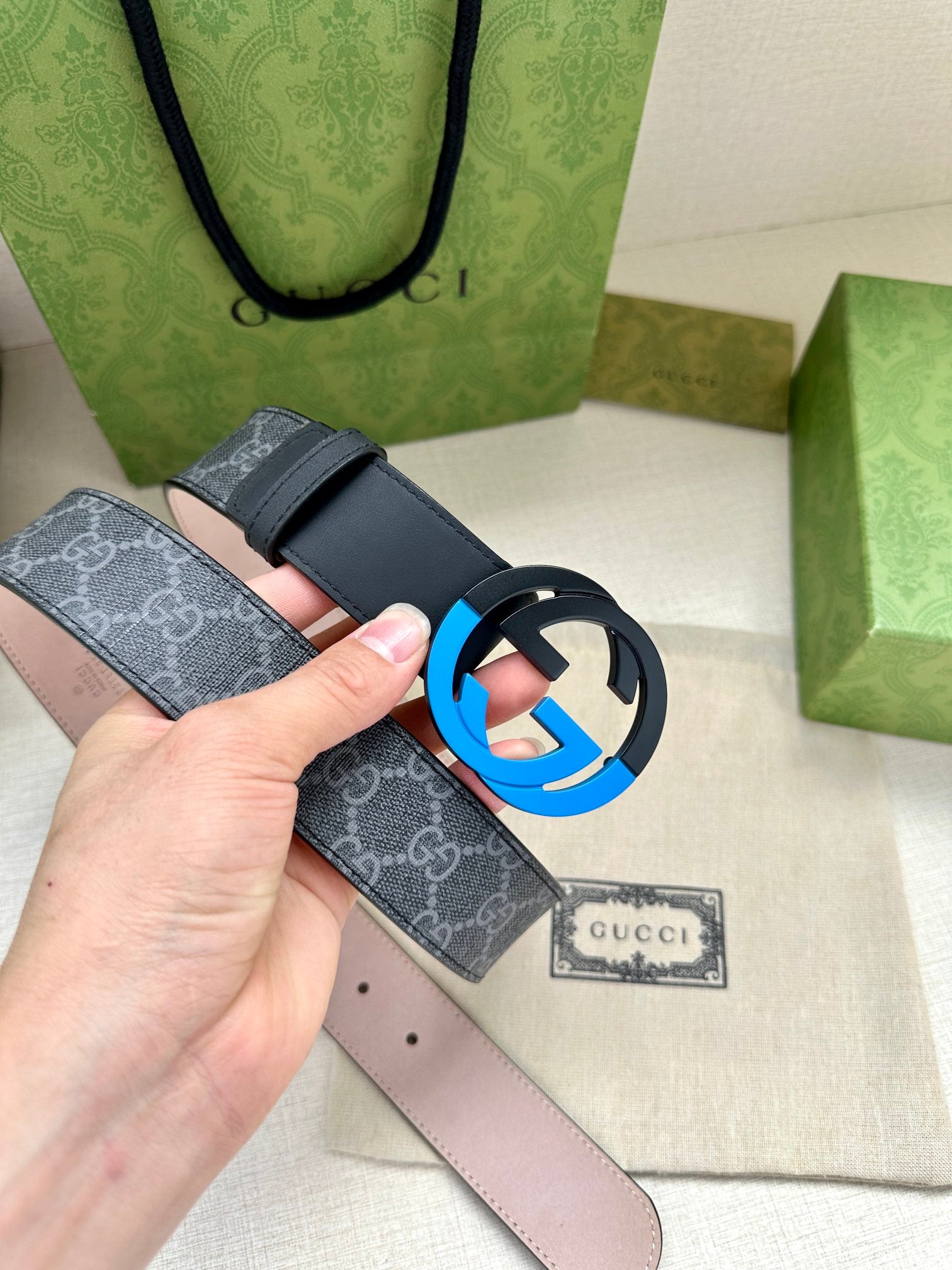 Designer belt with monogram panel and blue interlocking buckle, close-up in hand