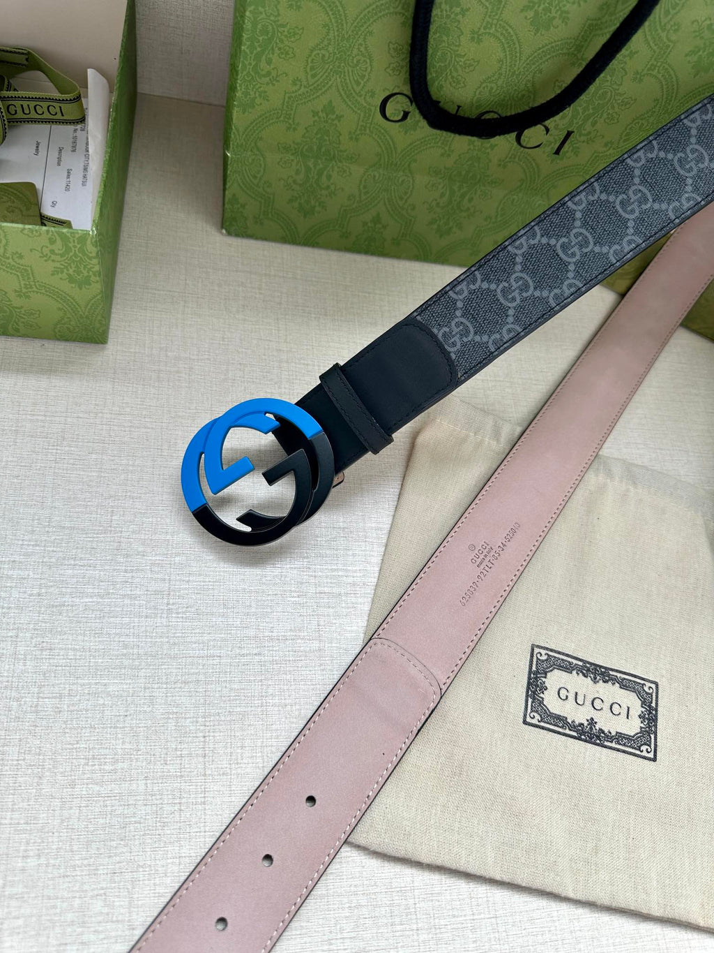 Designer belt with monogram strap and blue interlocking buckle, with light pink underside
