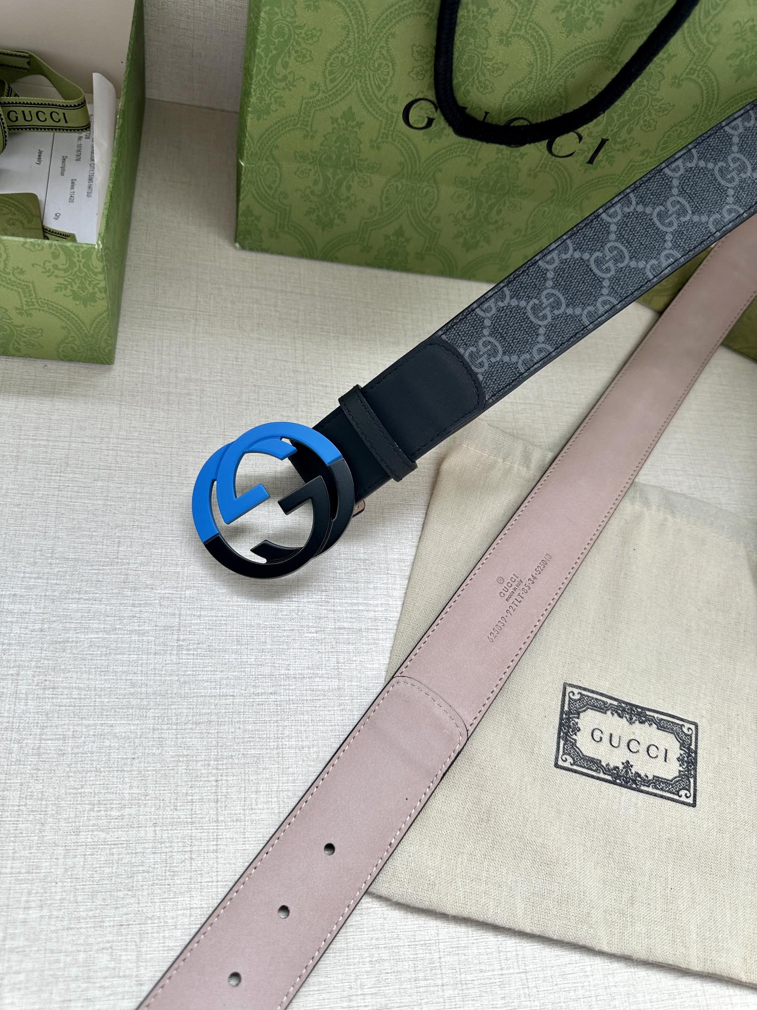 Designer belt with monogram strap and blue interlocking buckle, with light pink underside