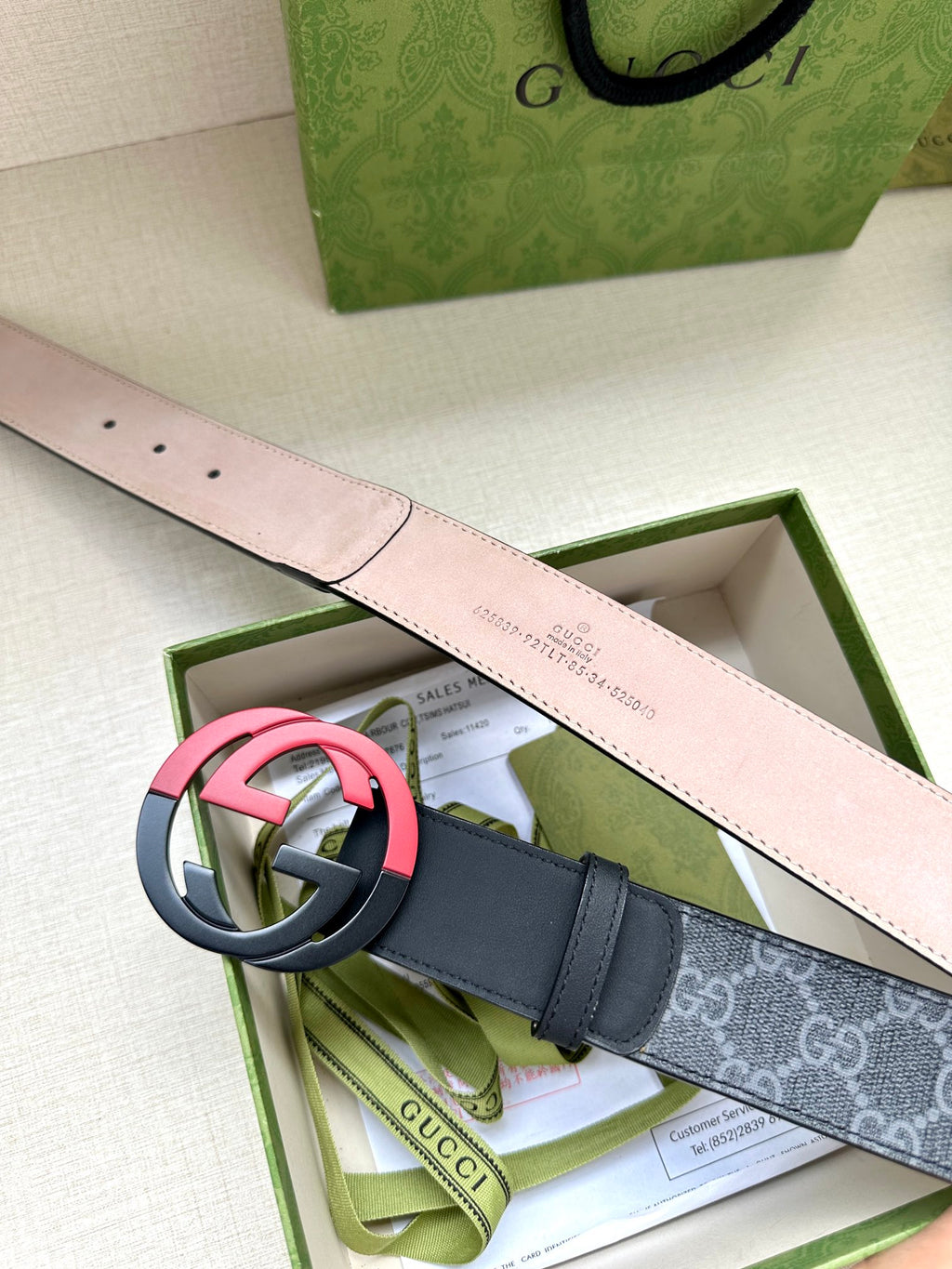 Designer belt with dark monogram strap and pink buckle, with light pink lining exposed