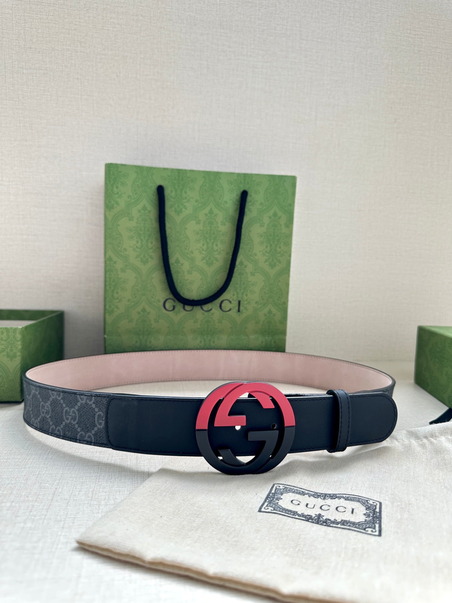 Designer belt with dark strap, monogram panel, and red interlocking buckle on display
