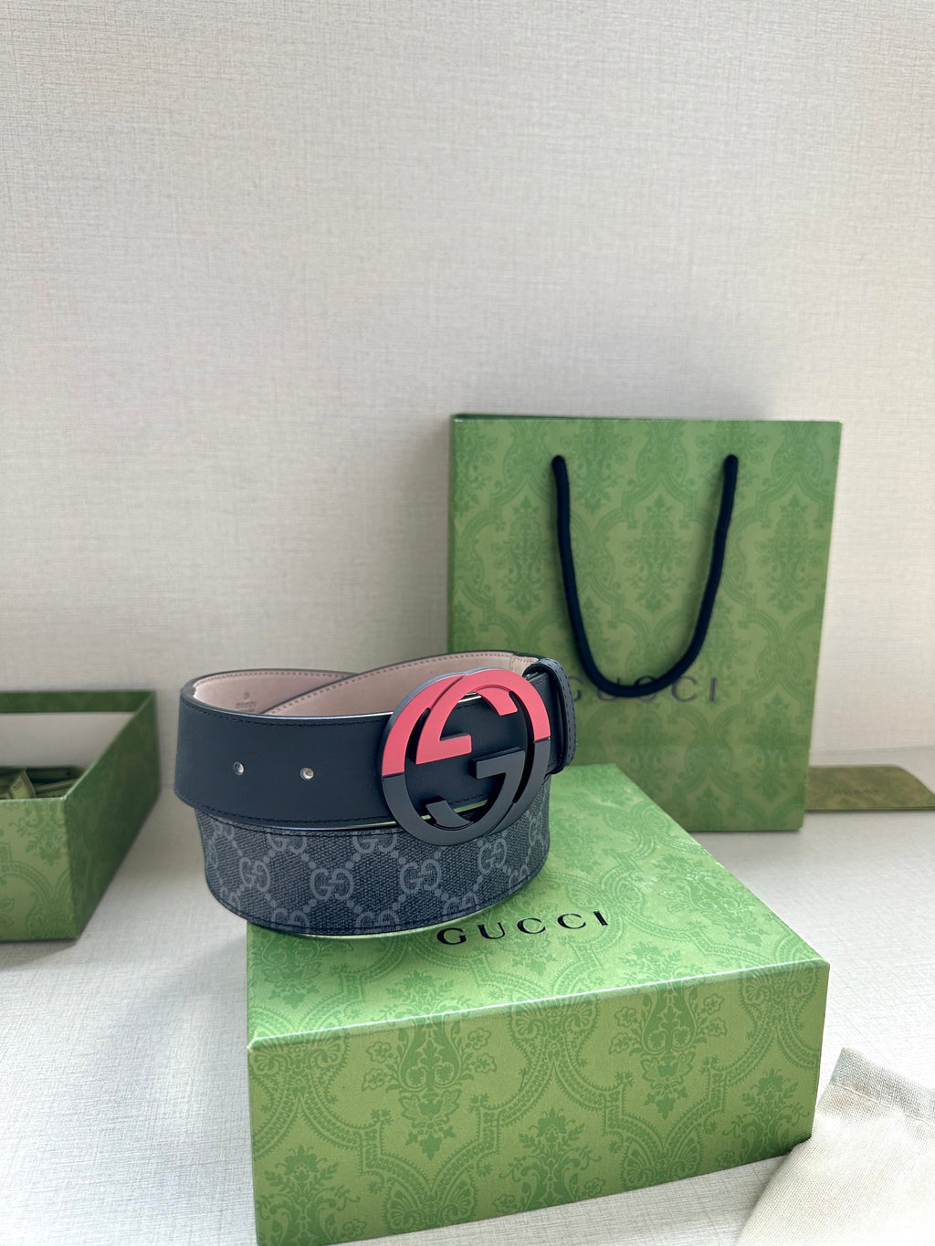 Designer belt with dark strap and pink interlocking buckle, shown on gift box