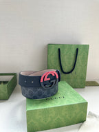 Designer belt with dark strap and pink interlocking buckle, shown on gift box