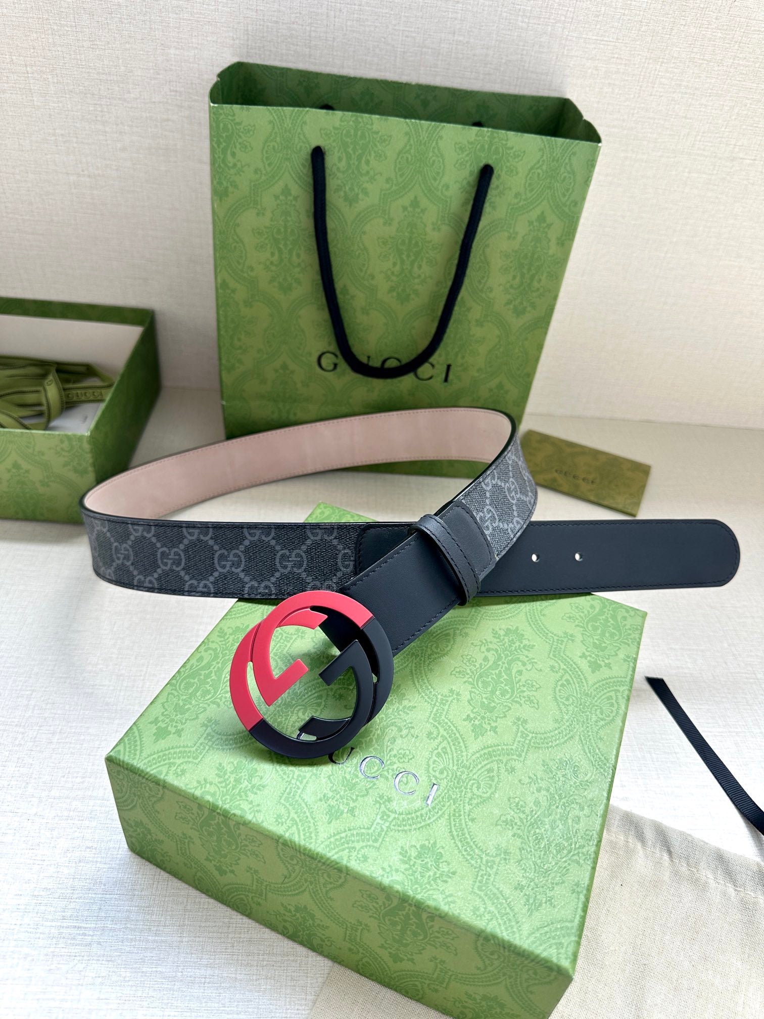 Designer belt with dark strap and pink interlocking buckle, shown with packaging