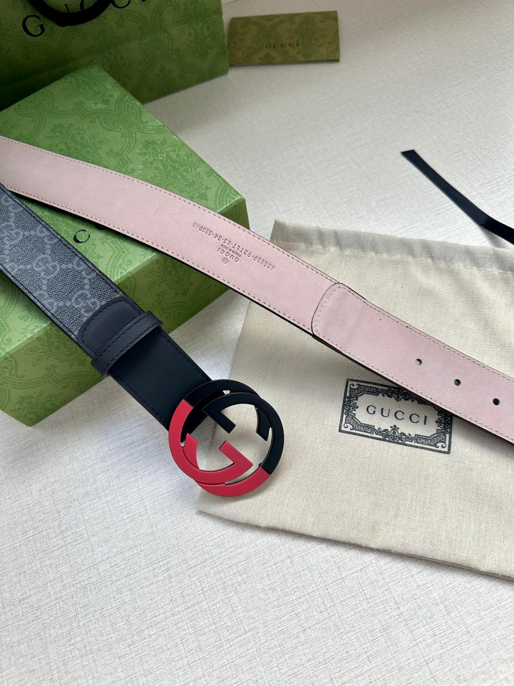 Designer belt with light pink underside and red interlocking buckle, angled view
