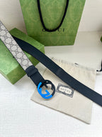 Designer belt with dark blue strap and round GG buckle on a gray canvas panel