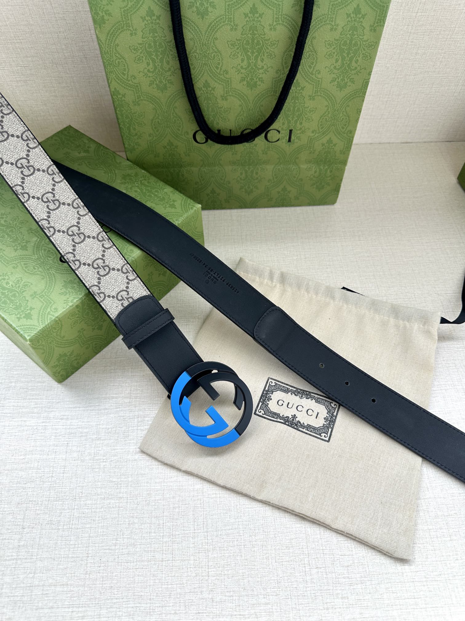 Designer belt with dark blue strap and round GG buckle on a gray canvas panel