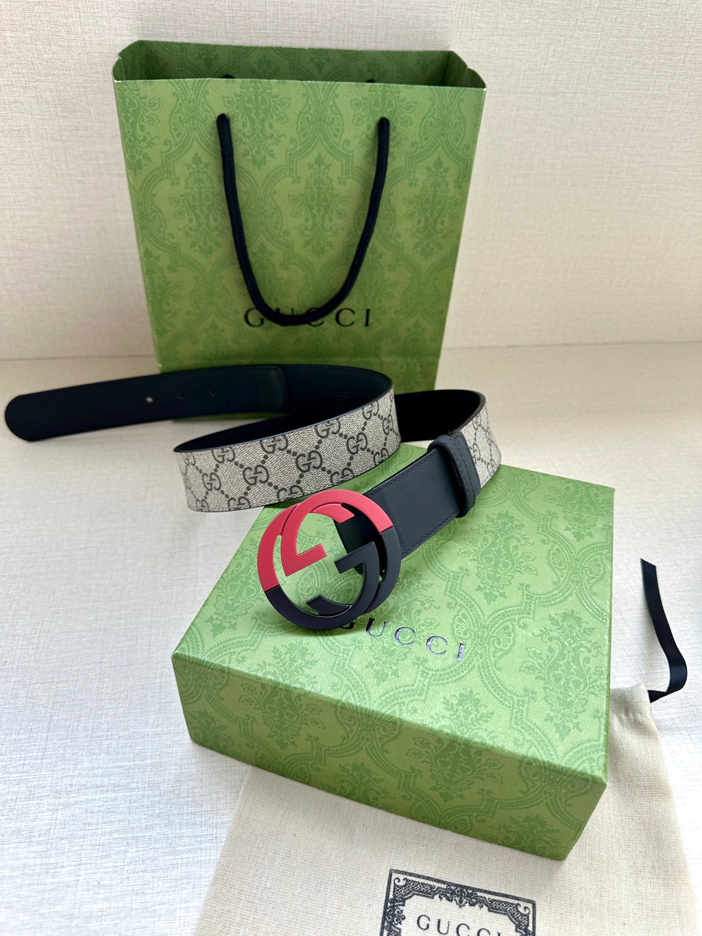 Designer belt with gray GG canvas, dark blue edges, and pink/red GG buckle