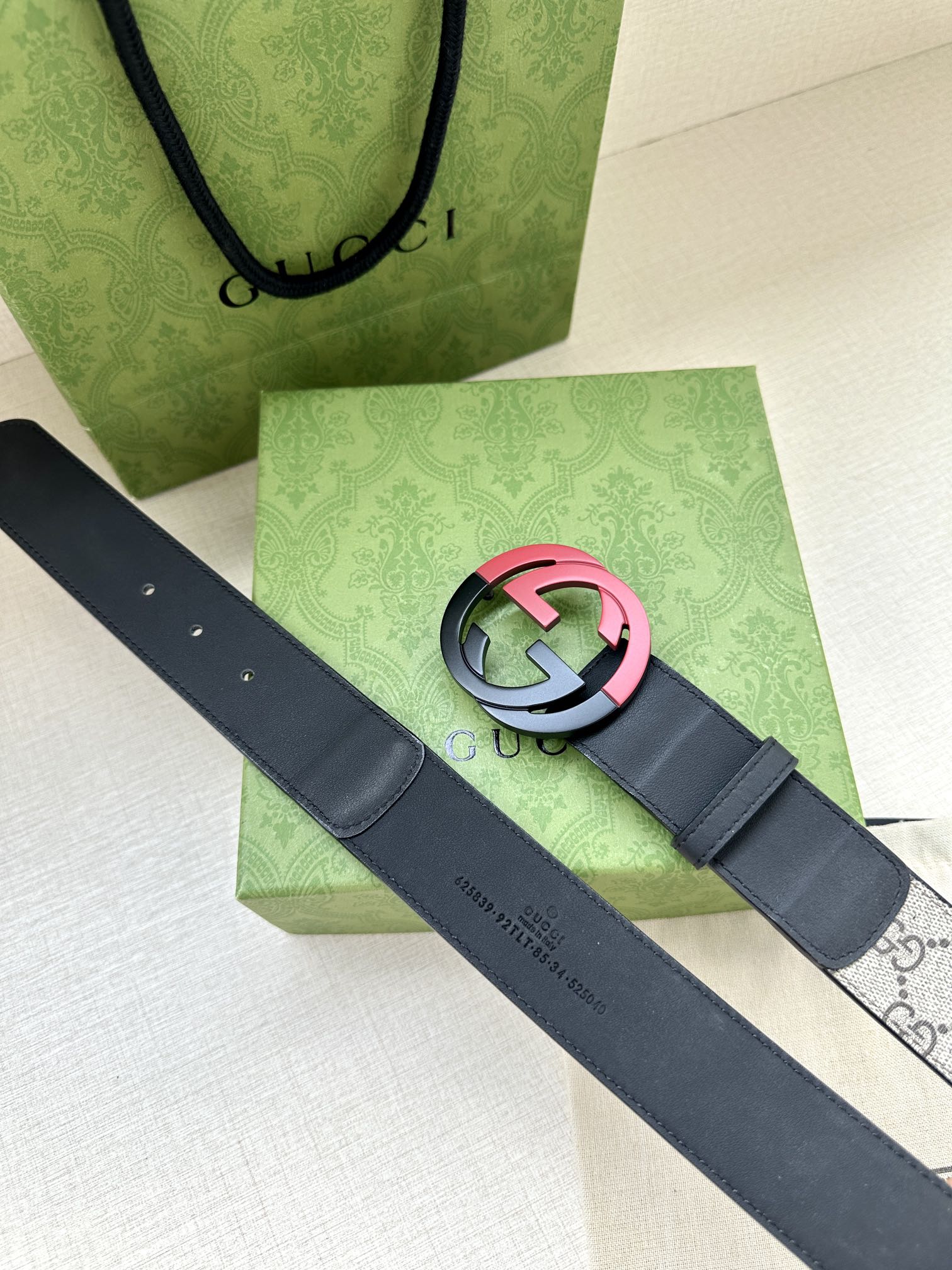 Designer belt with dark blue leather and pink/accent round GG buckle over gray strap