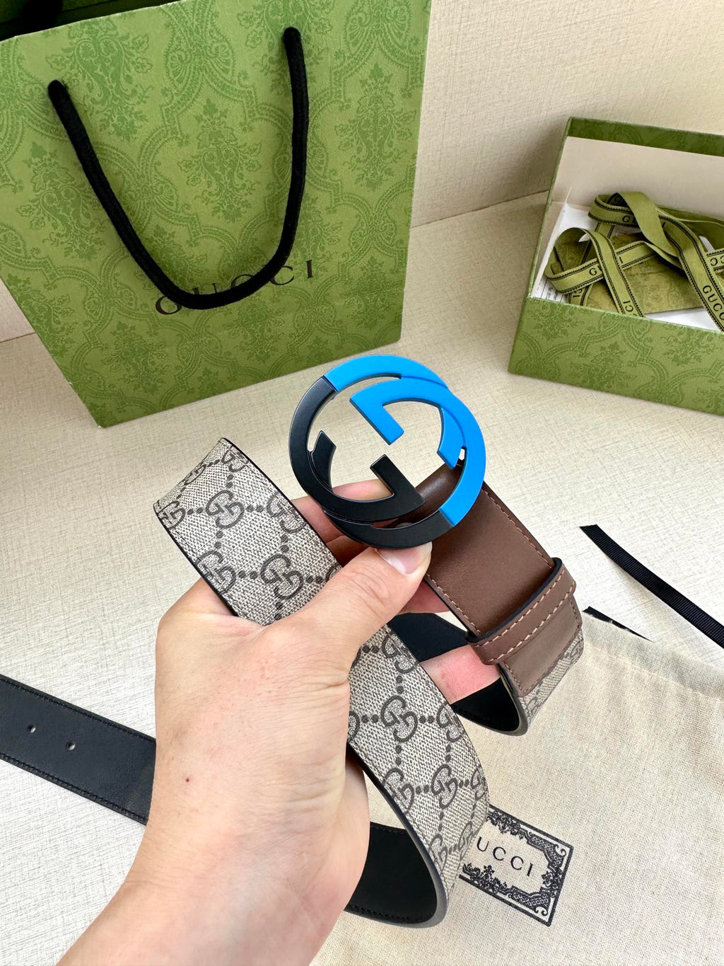 Beige GG-print belt with brown leather edges and round black buckle, held above pouch