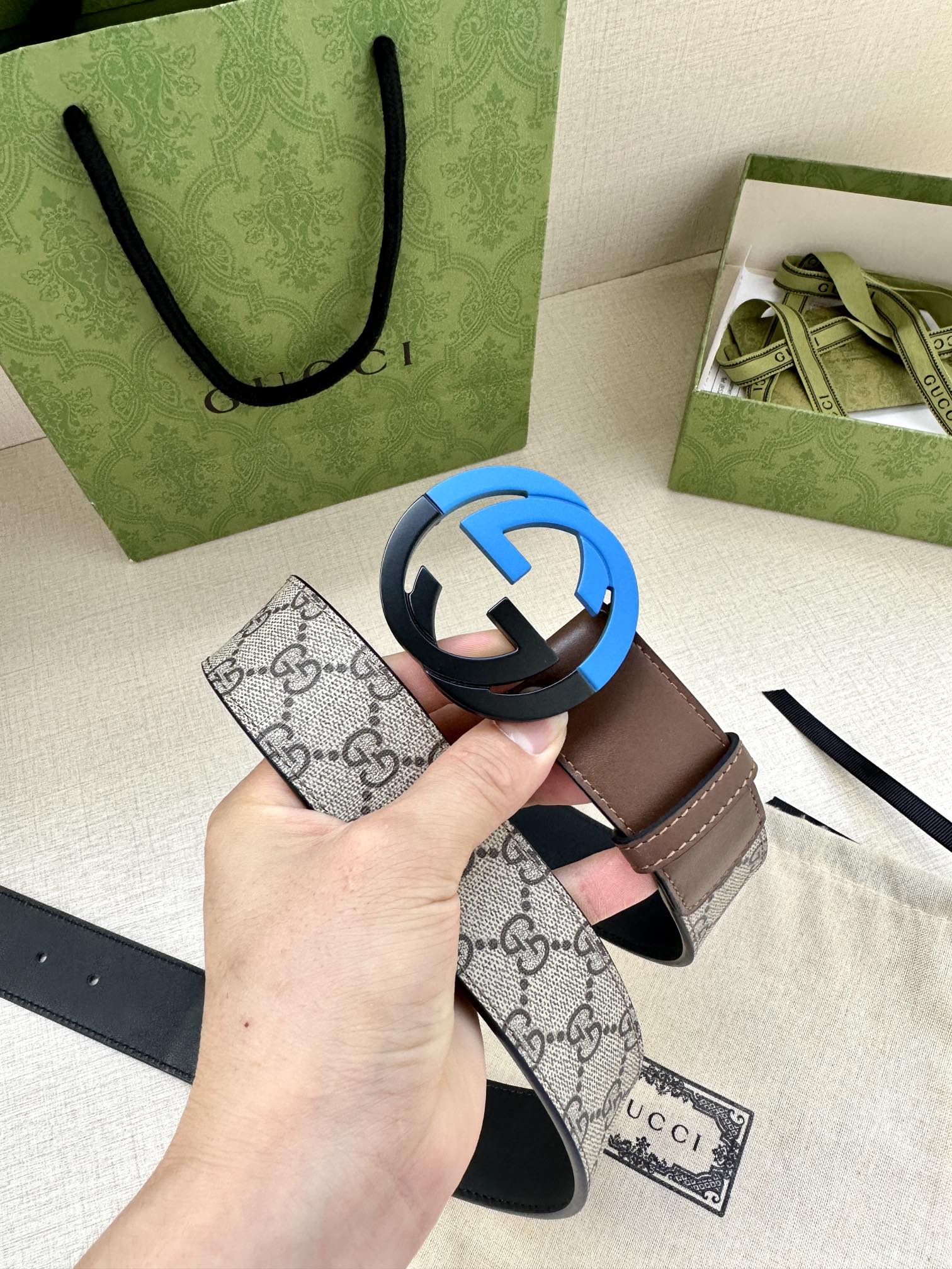 Beige GG-print belt with brown leather edges and round black buckle, held above pouch