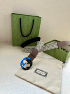 Brown leather and beige GG-print belt with round black buckle, resting across dust bag