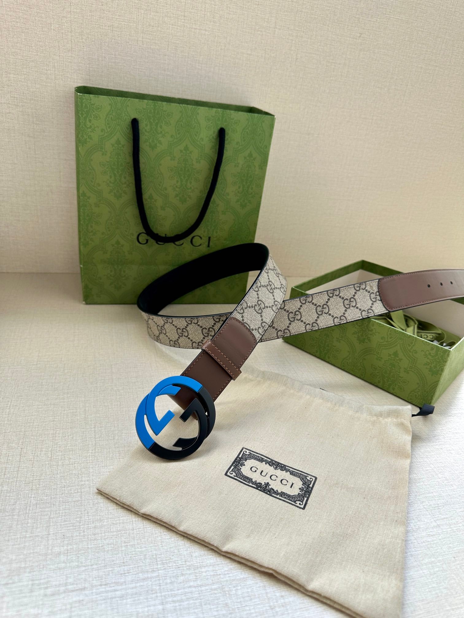 Brown leather and beige GG-print belt with round black buckle, resting across dust bag