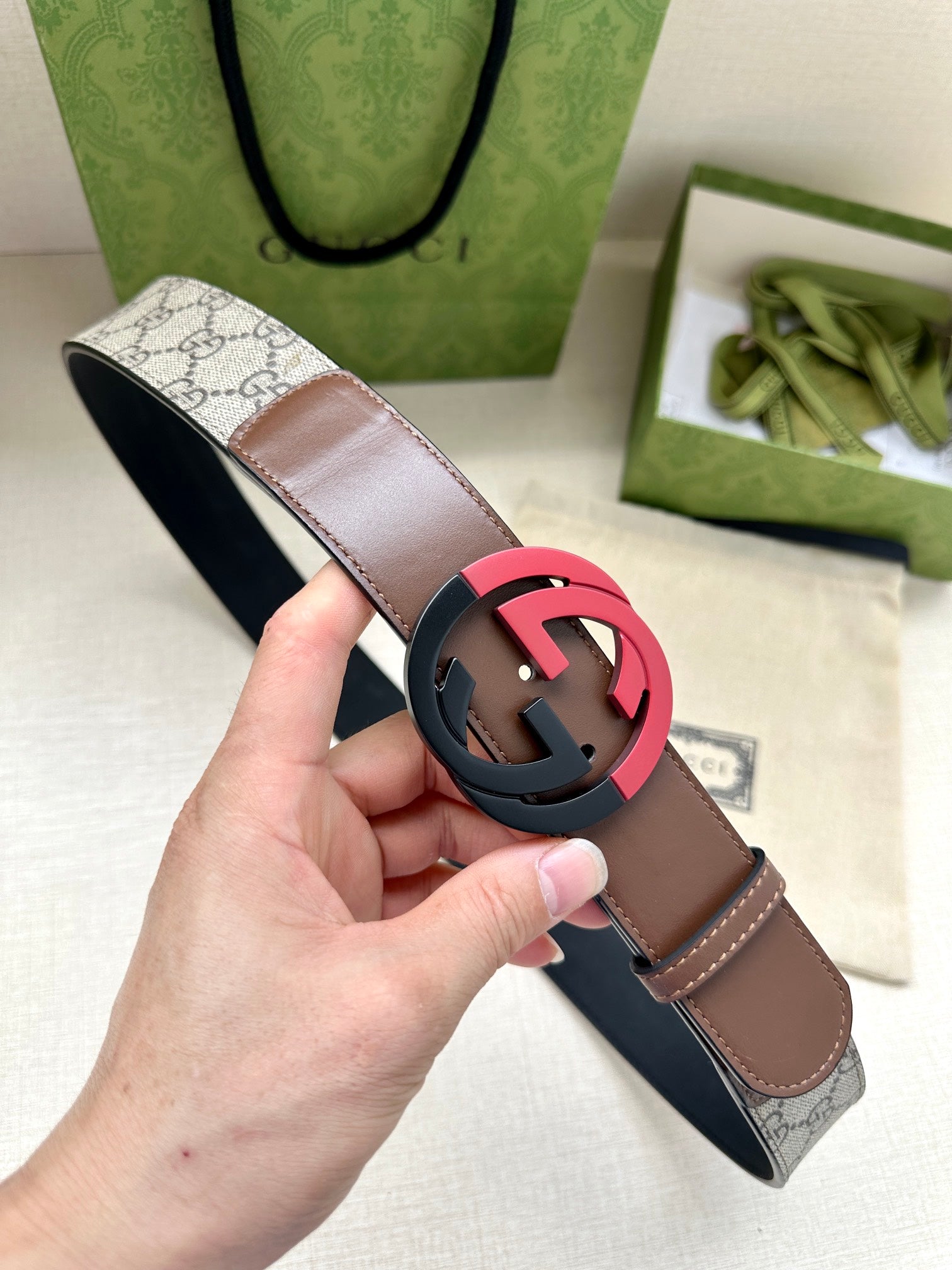 Brown leather belt with round black buckle and dark strap underside, shown in hand