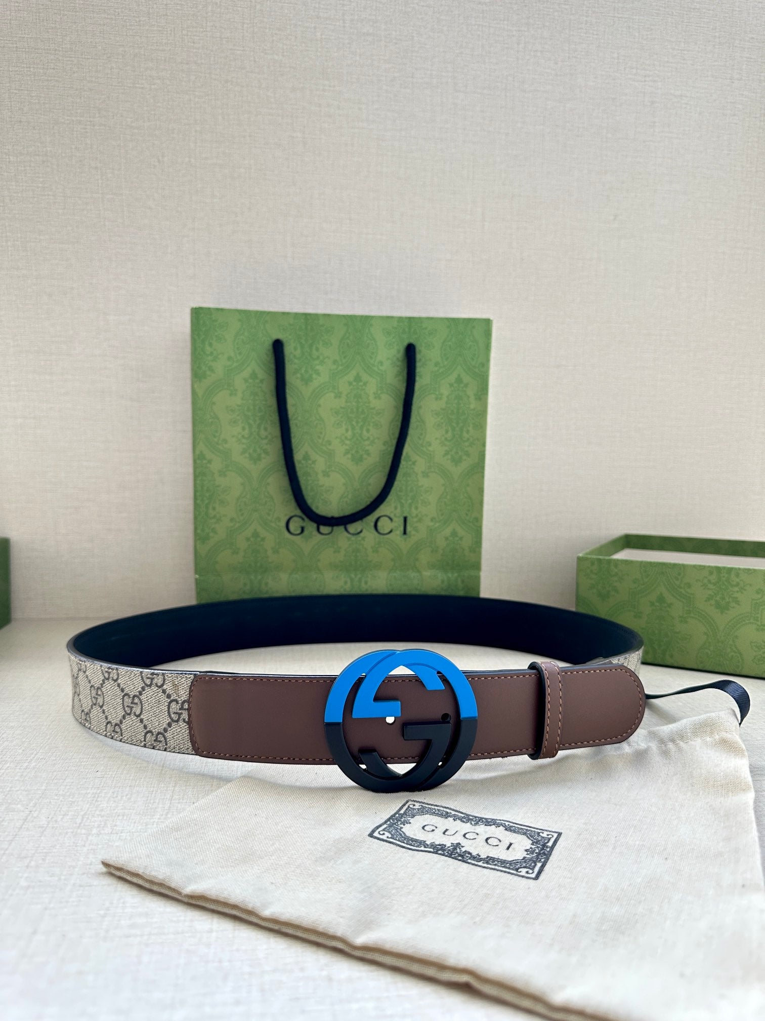 Brown leather belt with beige GG-print side and round black buckle, laid on pouch