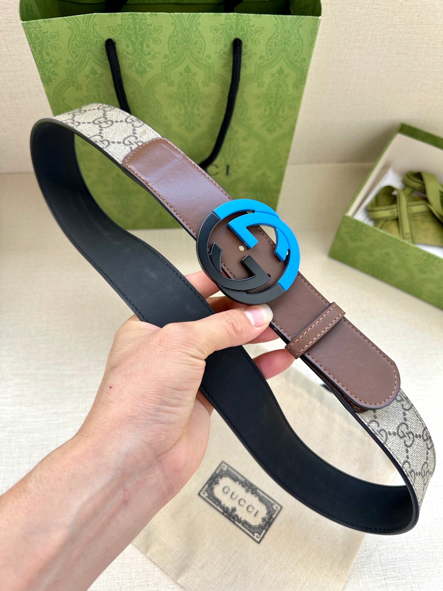Brown and beige GG-print belt with round black buckle and dark underside, handheld