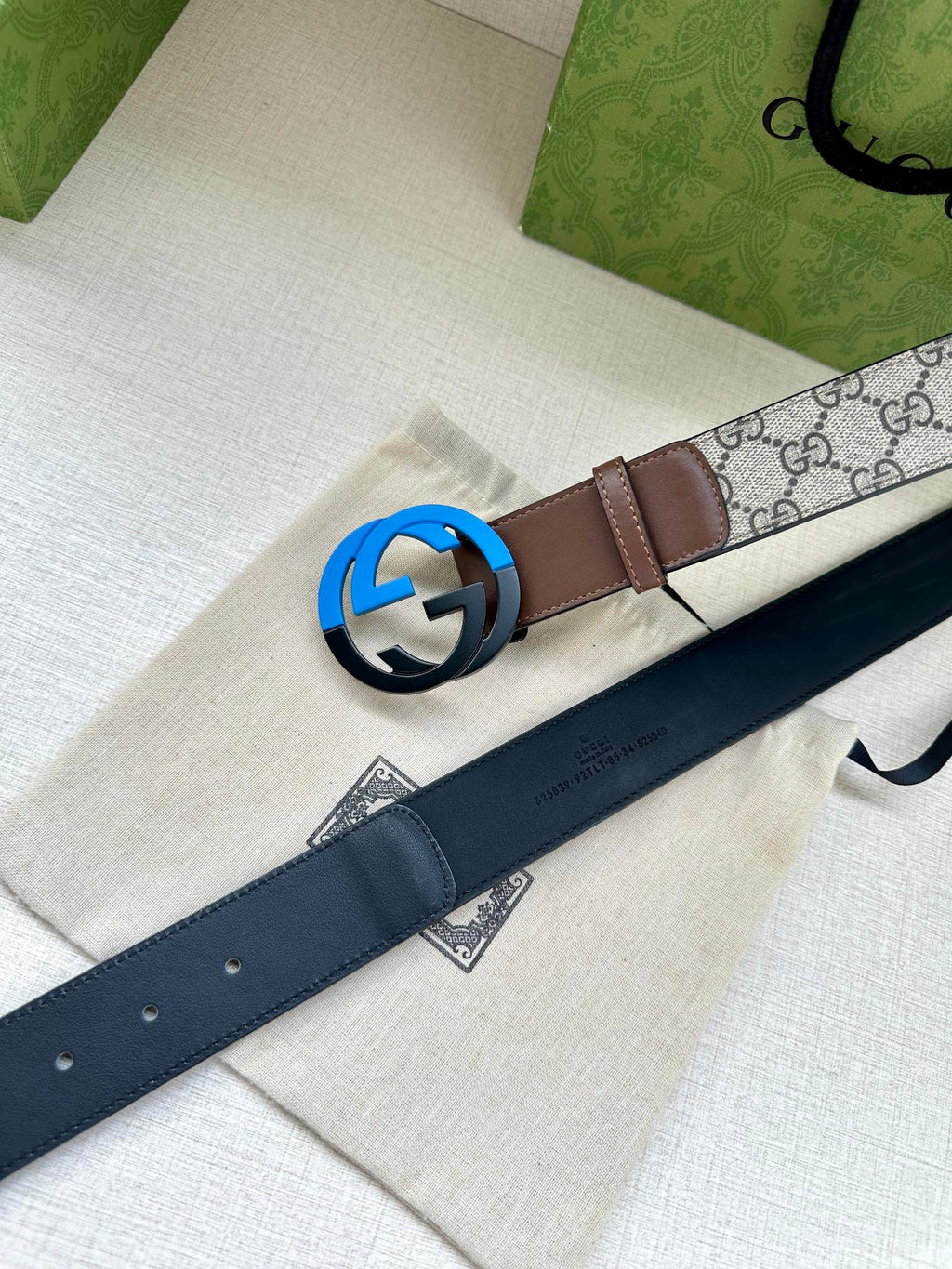 Brown leather belt with round black buckle beside dark navy strap on dust bag