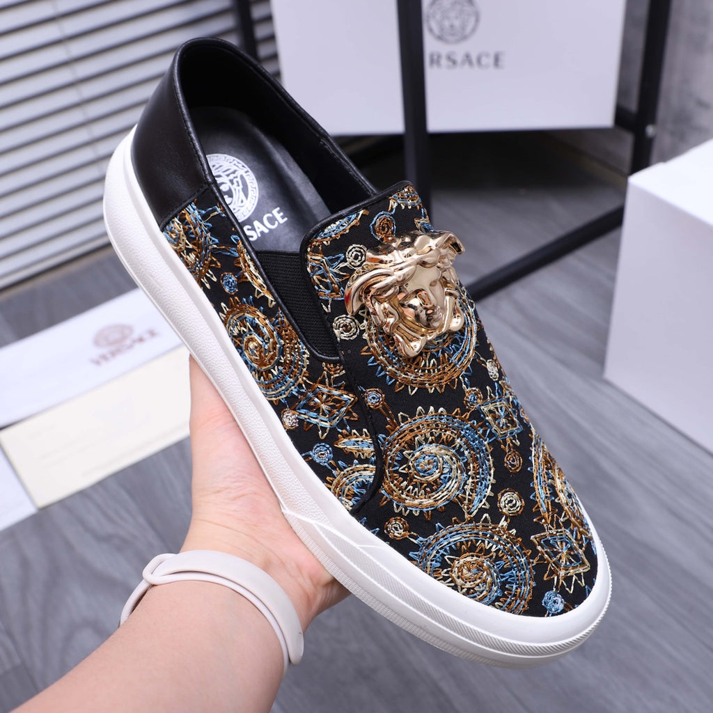 Versace slip-on sneaker on hand, dark fabric upper with gold and blue medallion print, white sole