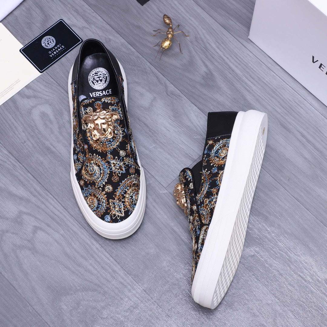 Versace slip-on sneaker angle view, dark patterned upper with gold ornament, white sidewall sole