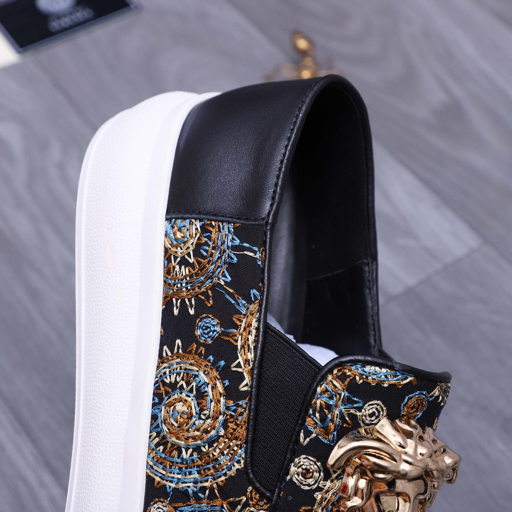 Versace slip-on sneaker close-up, dark upper with gold ornament and blue pattern, white sole
