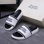 Alexander McQUEEN slide sandals on floor, white footbed with black strap bands