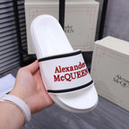 White slide sandal with black trim band and red Alexander McQUEEN on strap