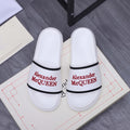 White slide sandals with black strap trim and red Alexander McQUEEN logo