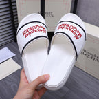 White slide sandals held open, showing red Alexander McQUEEN logo on footbed