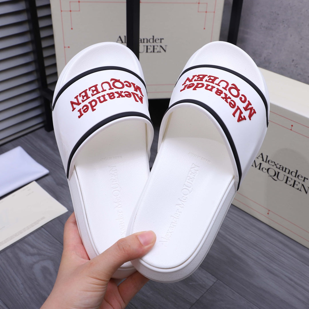 White slide sandals held open, showing red Alexander McQUEEN logo on footbed