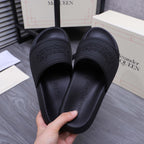 Alexander McQueen black slide sandals, hand holding one with logo-embossed footbed