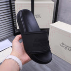 Alexander McQueen black slide sandal held in hand, embossed logo on strap