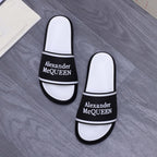 Two white slide sandals with black Alexander McQueen logo band and trim