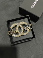 Gold-tone Chanel brooch with pearl and crystal accents, full script logo view