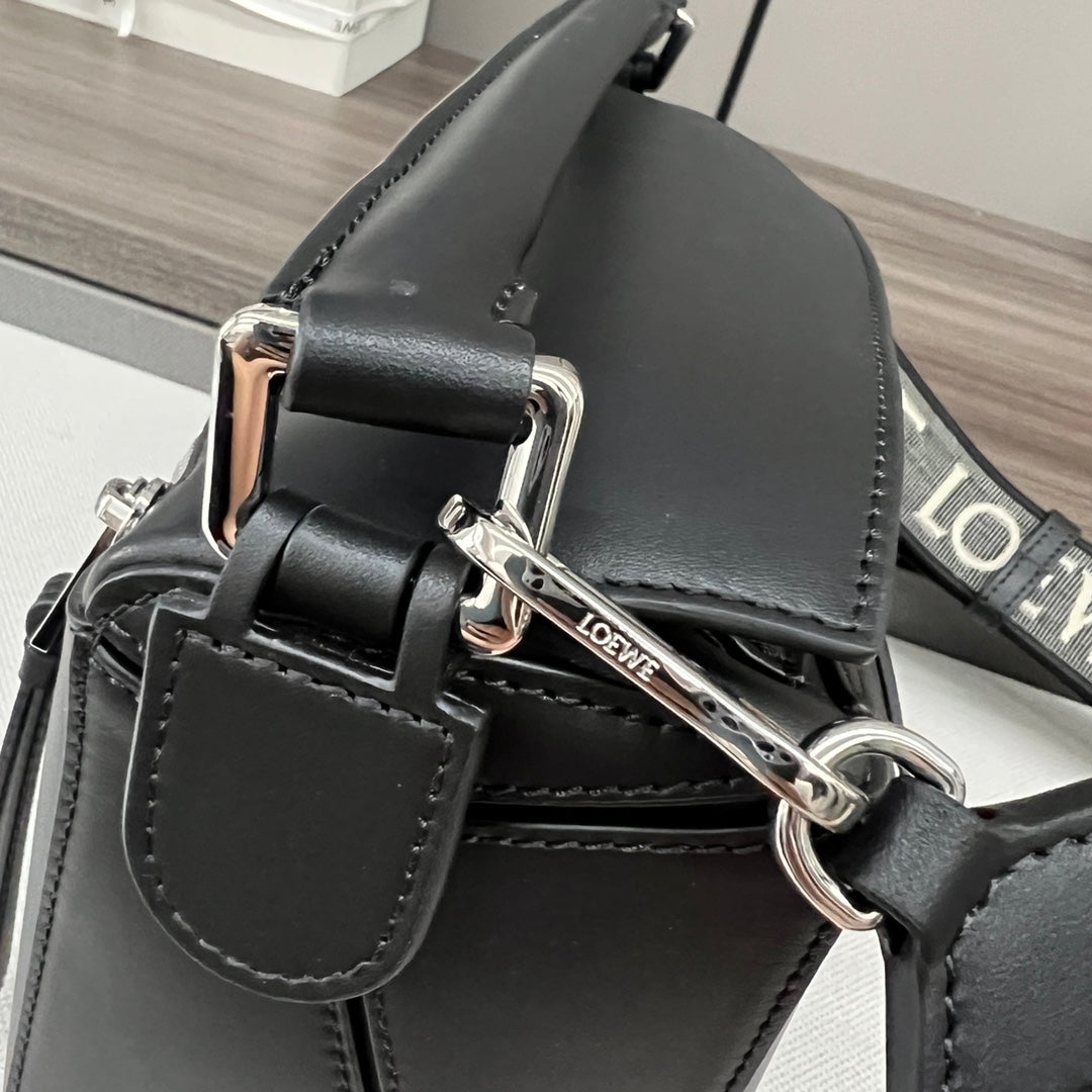 Close-up of black leather bag with adjustable strap and silver buckles.