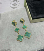 Clover drop earrings with green enamel and gold-tone chain, lying on display surface