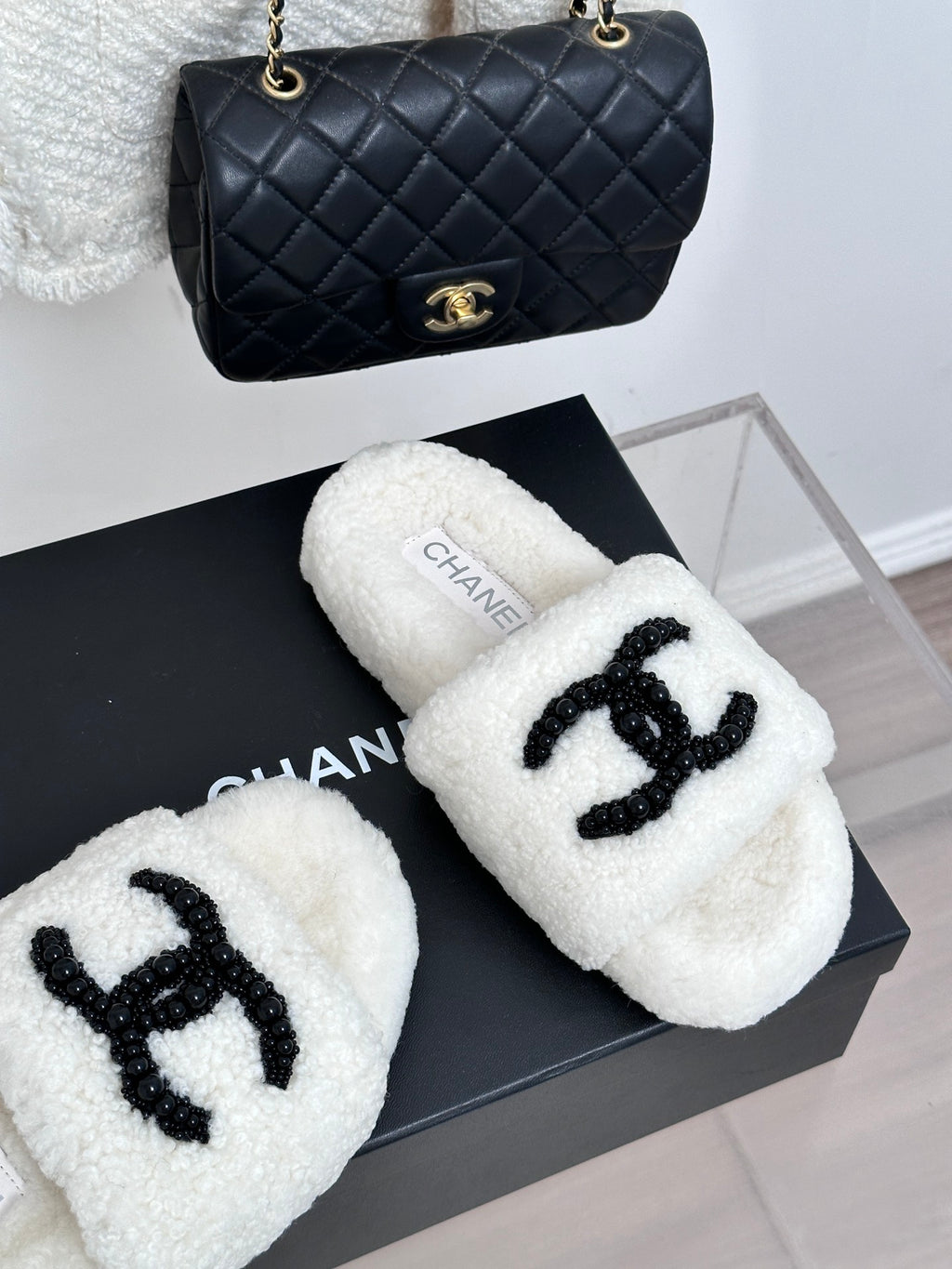 Chanel white fuzzy slides with black CC emblem, angled pair on box