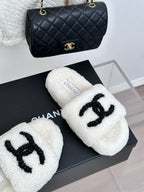Chanel white fuzzy slides with black CC emblem, angled pair on box