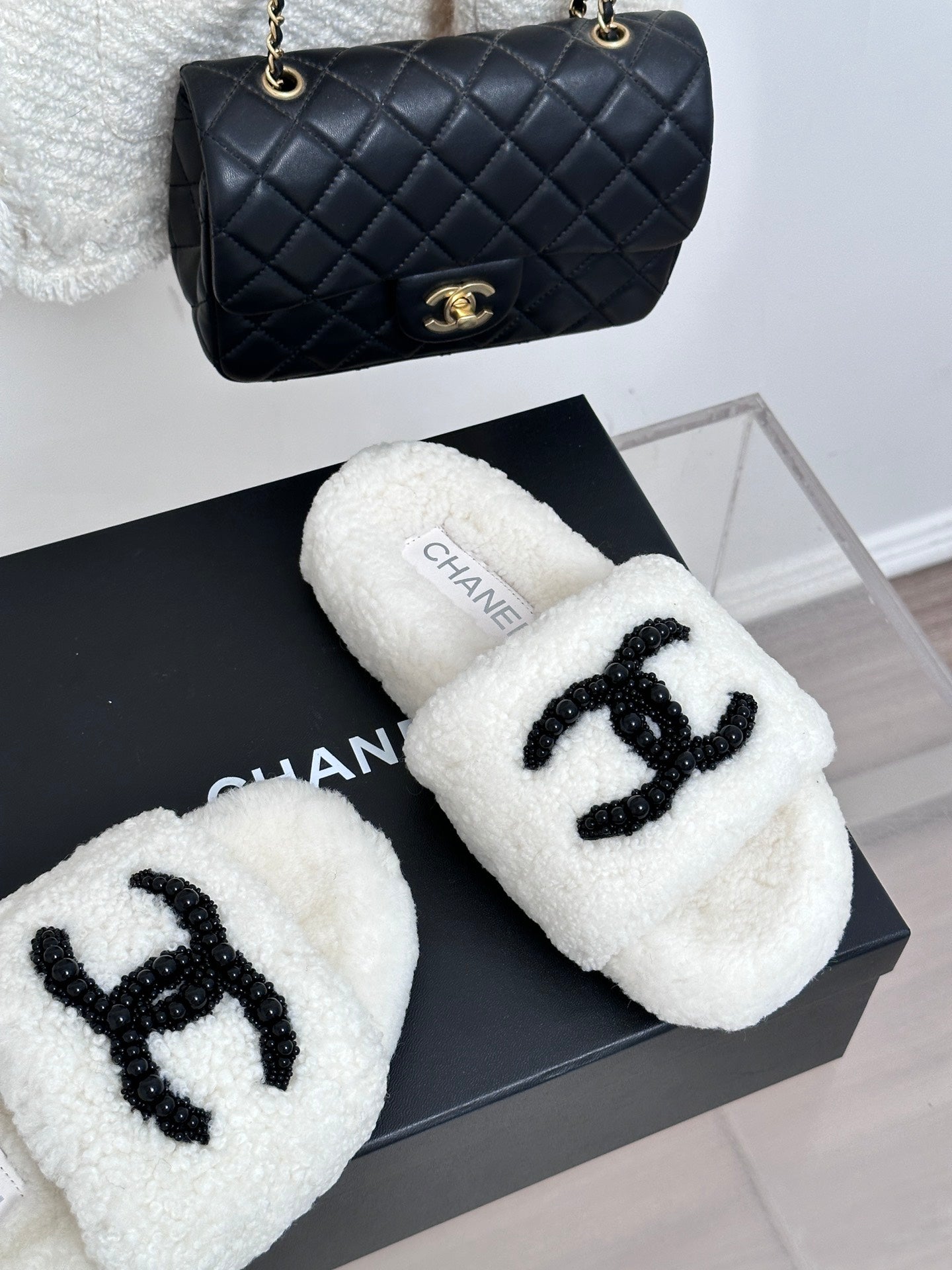 Chanel white fuzzy slides with black CC emblem, angled pair on box