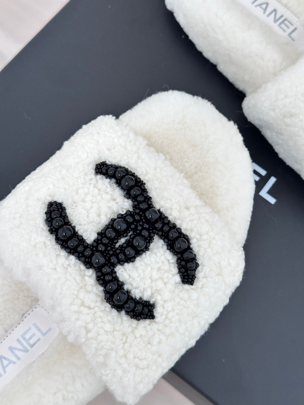 Chanel white fuzzy slides with black CC emblem, close-up logo detail