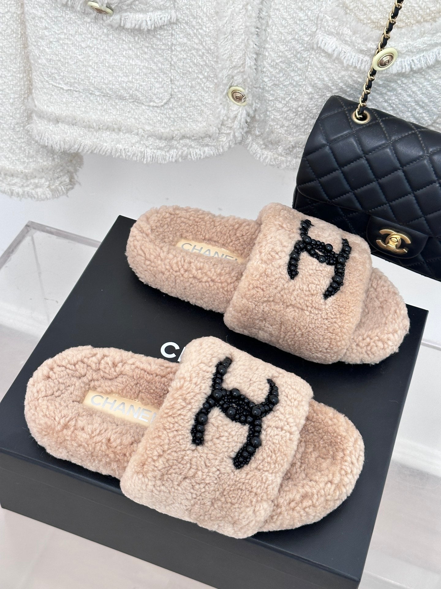 Pair of beige plush slides with black beaded logo on top, womens luxury shoes